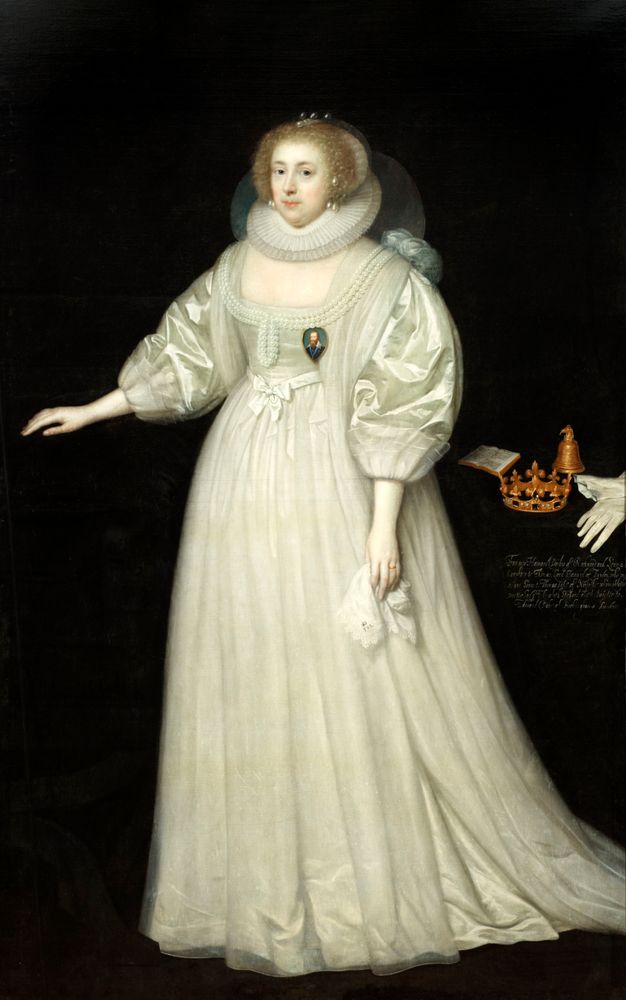 Painting. A pale-skinned woman wears a long, voluminous white gown against a black background in this full-length portrait. Pearls line her headdress and neckline, and hang from her ears over a pleated ruff. A miniature she wears on her chest, shows a man in an oval that comes to a point at the bottom.